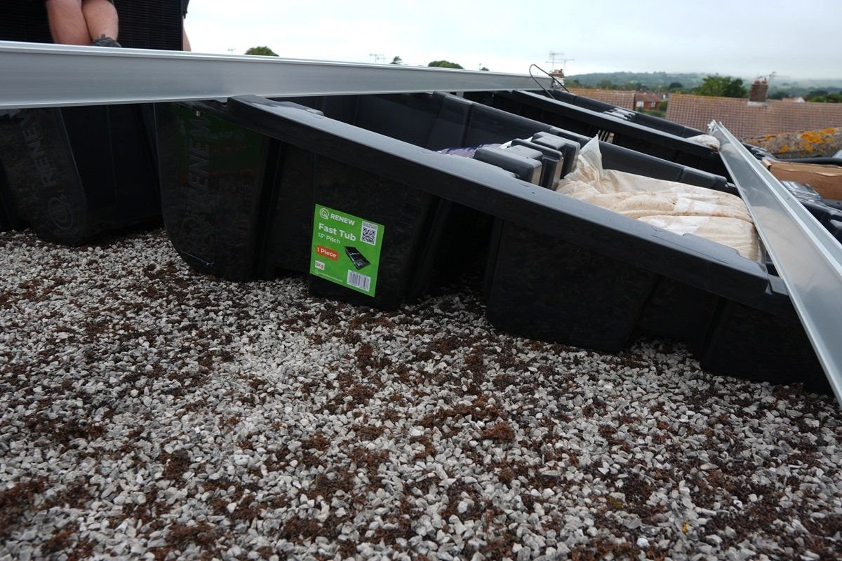 Close-up of Fast Tub units sitting on a gravel flat roof, with an aluminium rail being lowered onto the tub upstands